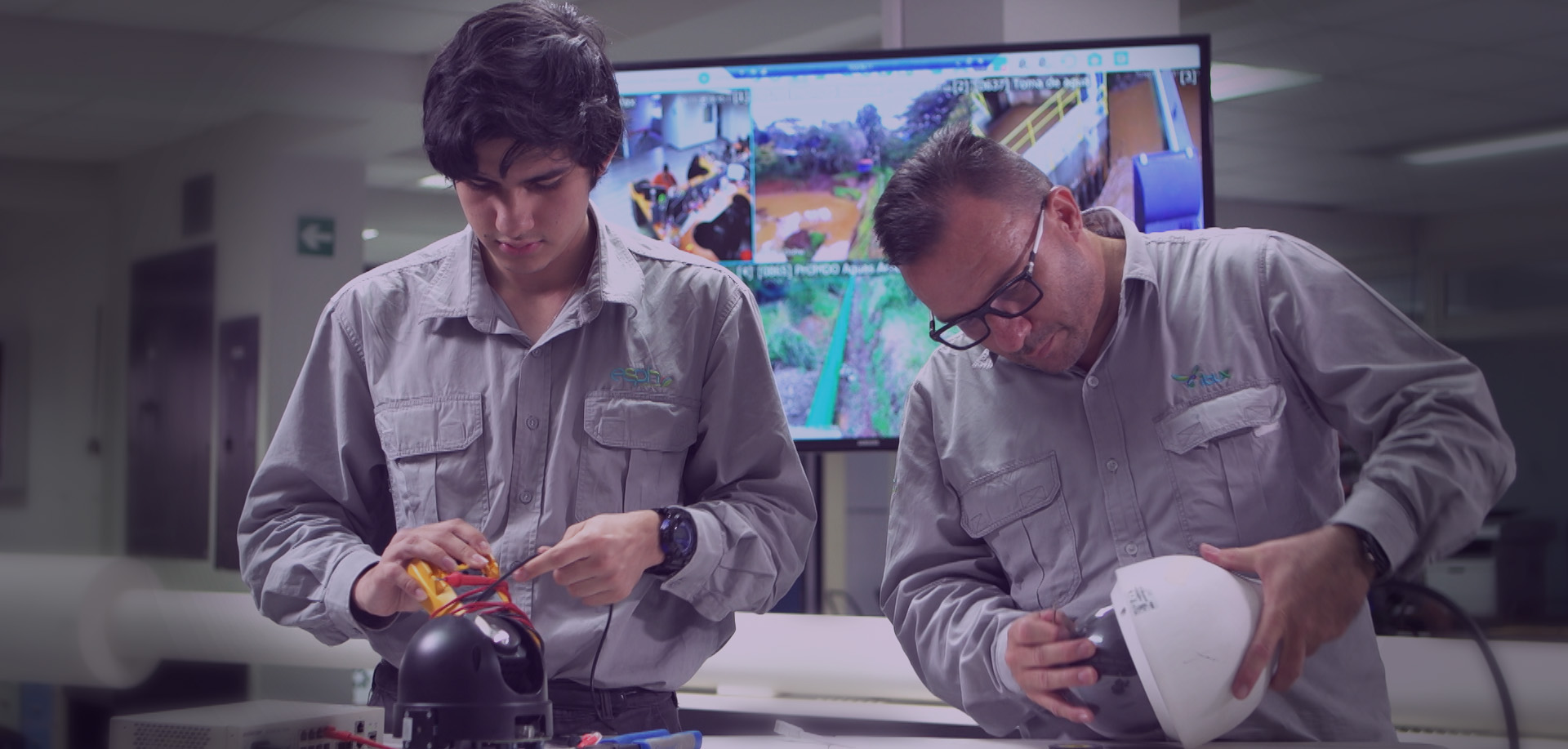 Dos hombres técnicos de Ibux revisar una cámara de seguridad cada uno dentro de un espacio de oficina