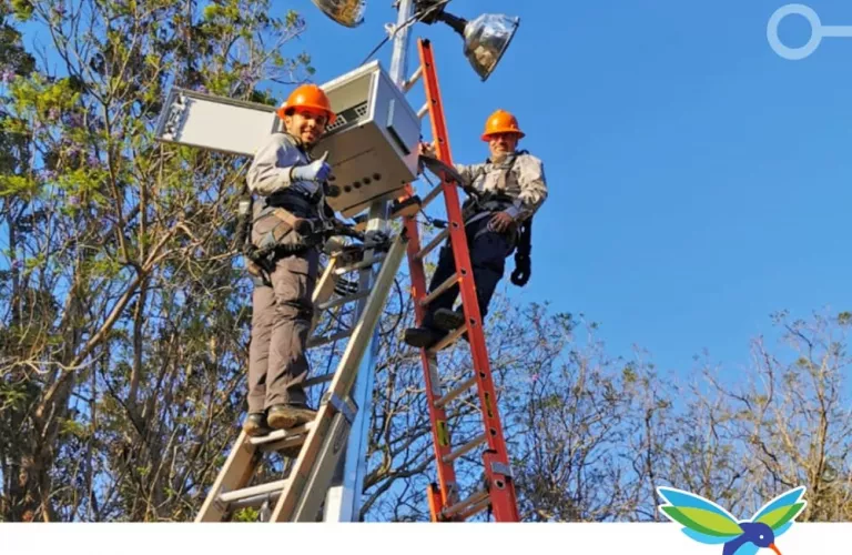 Dos trabajadores sobre escaleras apoyados en un poste de luz, sonriendo durante la instalación de equipo de video vigilancia