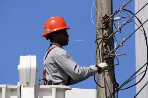 Colaborador de Ibux con casco naranja, arreglando cables eléctricos en un poste subido en una grua