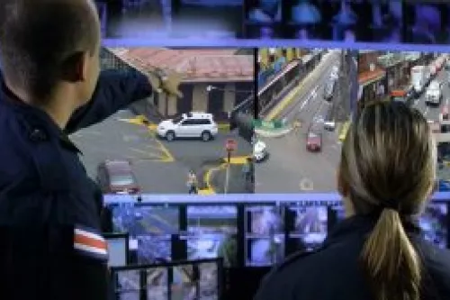 Hombre y mujer con uniforme policial observando monitor con imágenes de cámaras de video vigilancia